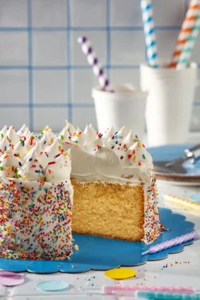 Torta de cumpleaños infantil con crema, granas y decoraciones coloridas.